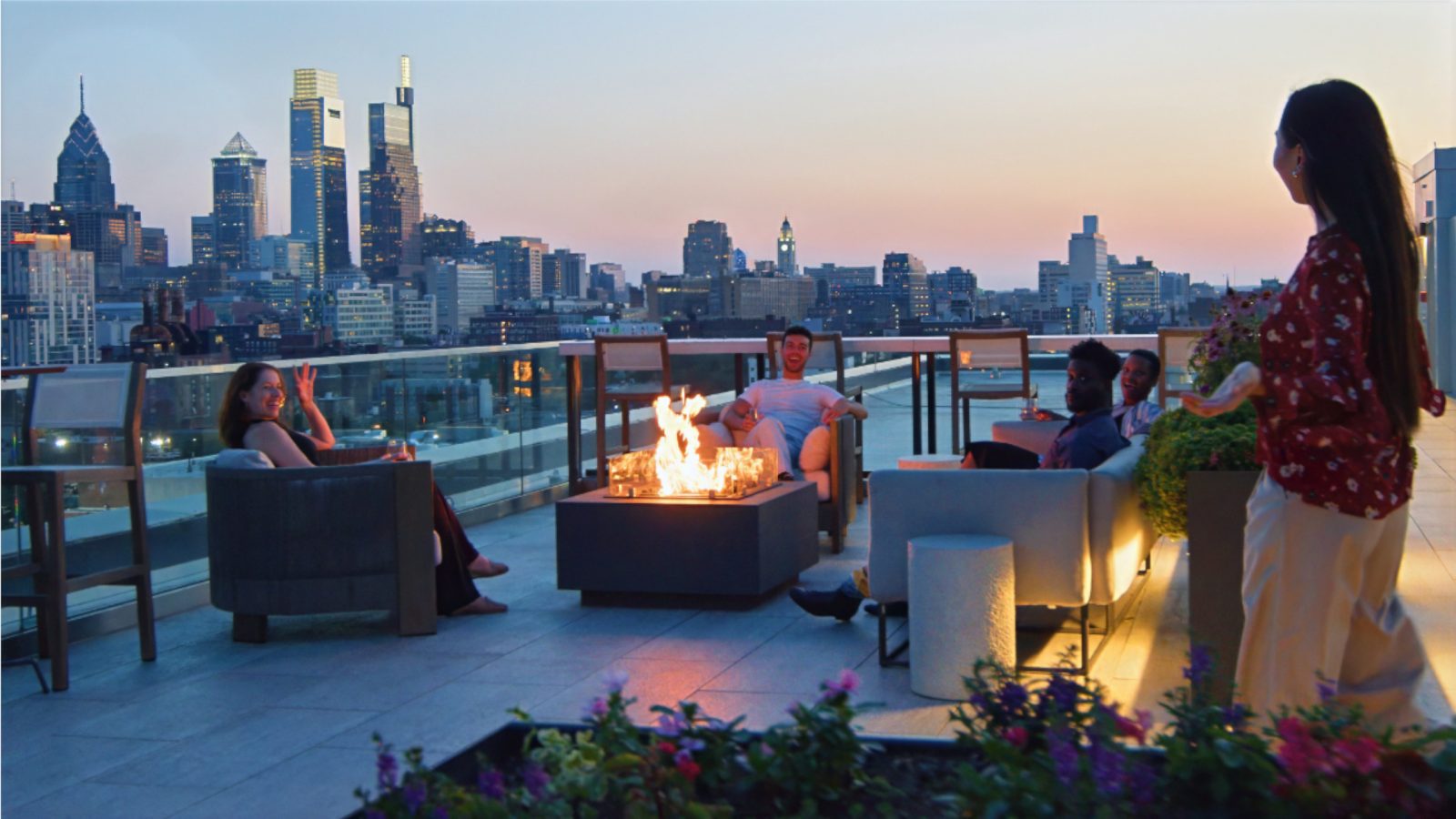 Group sitting around a rooftop fire pit at sunset.